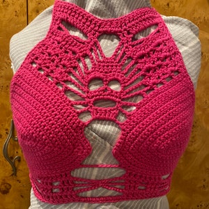 May include: A pink crocheted halter top with a geometric design and cutouts. The top is made with a fine yarn and has a delicate, feminine look.