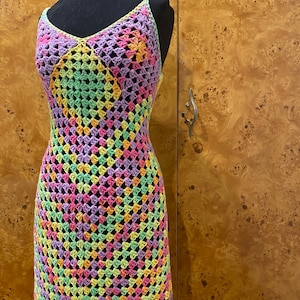 Puede incluir: Un vestido de crochet colorido con un patrón geométrico en tonos de rosa, verde, amarillo y morado. El vestido es sin mangas y tiene un escote en V.