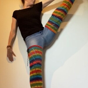 Puede incluir: Una persona que lleva una camisa negra y pantalones vaqueros azules con un calienta piernas de crochet de colores en su pierna derecha. El calienta piernas es un arco&iacute;ris de colores y tiene un patr&oacute;n de crochet.