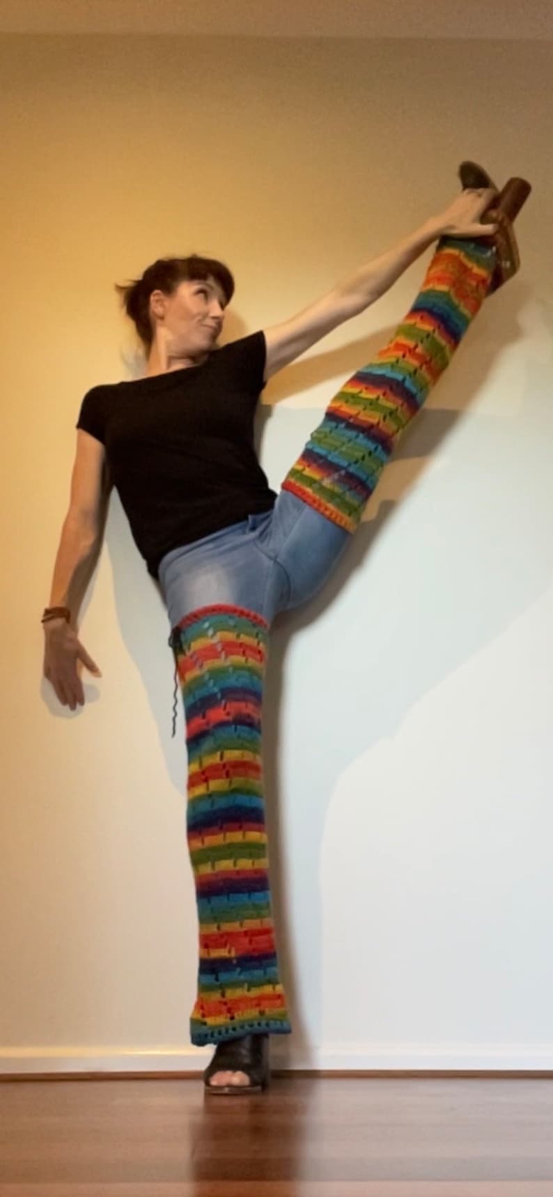 Puede incluir: Una persona que lleva una camisa negra y pantalones vaqueros azules con un calienta piernas de crochet de colores en su pierna derecha. El calienta piernas es un arco&iacute;ris de colores y tiene un patr&oacute;n de crochet.