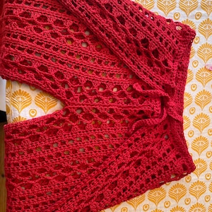 May include: Red crochet pants with a loose, flowy fit. The pants have a wide leg and a tie at the waist.