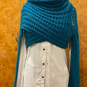 Può includere: Un scialle all'uncinetto blu turchese con un motivo traforato. Lo scialle è drappeggiato su una camicia bianca con bottoni.