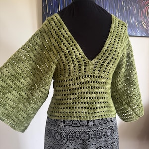 May include: A green crocheted top with a V-neck and 3/4 sleeves. The top is made with a lacy stitch and has a loose fit.