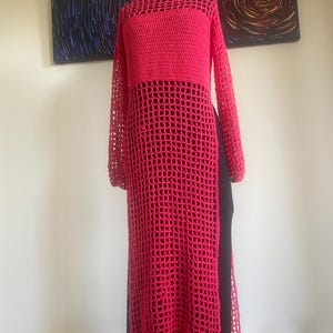 以下が含まれることがあります： ゆったりとしたフィット感と広く開いたネックラインを持つ、長いピンクのクロシェチュニック。チュニックはメッシュパターンと長袖です。