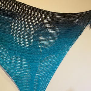 May include: A teal and black crocheted shawl with a gradient pattern. The shawl is made of a lightweight, open-weave fabric.