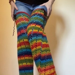Puede incluir: Un par de polainas de crochet a rayas arco&iacute;ris con un patr&oacute;n de encaje. Las polainas se llevan sobre unos vaqueros azules.