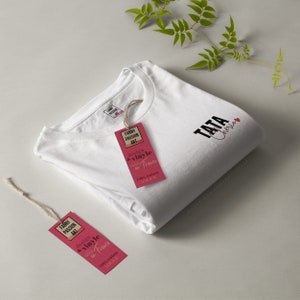 May include: White t-shirt with black text that says "TATA Cherie" and a red heart. The shirt is folded and has a red and white tag attached that says "FANNY PASSION ART design & vinyle en France 100% coton".