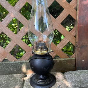 May include: A black oil lamp with a clear glass chimney. The lamp has a round base and a simple design.