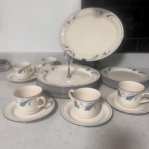 May include: A set of white ceramic dinnerware with a blue and red floral design. The set includes plates, cups, and saucers.