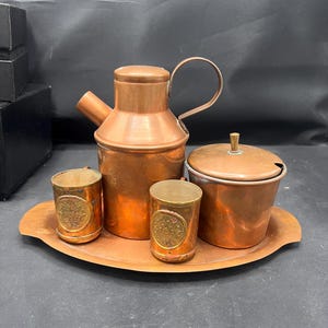 May include: A copper serving set with a pitcher, two cups, a sugar bowl, and a tray. The set has an ornate design and is perfect for serving coffee or tea.