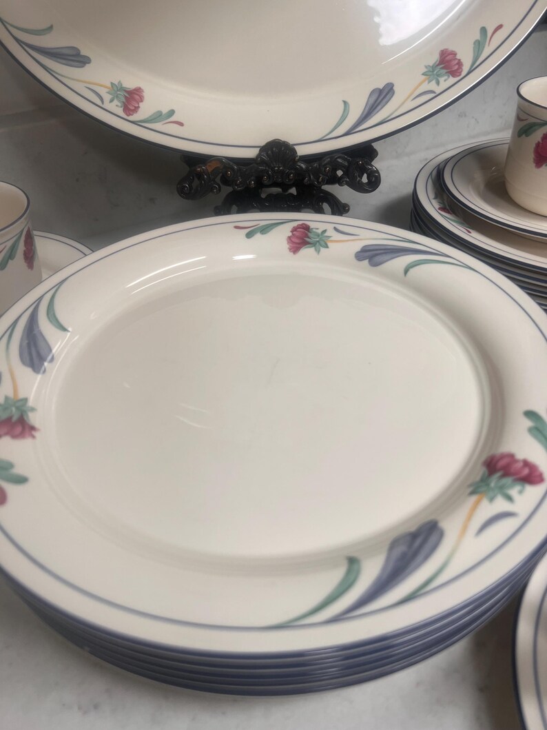 May include: A set of white ceramic dinner plates with a blue and green floral design. The plates have a blue rim and a white center.