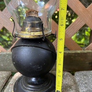 May include: A black oil lamp with a glass chimney and a brass burner. The lamp is about 7 inches tall.