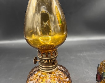 May include: A small amber glass oil lamp with a fluted base and a clear glass chimney. The lamp has a brass wick adjuster and a brass cap.