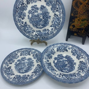 May include: Three blue and white porcelain plates with a floral pattern and a cottage scene. The plates are in different sizes, with the largest plate in the back and the smallest plate in the front.