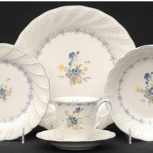 May include: A set of white porcelain dinnerware with a blue and floral pattern. The set includes a dinner plate, salad plate, soup bowl, teacup, and saucer.