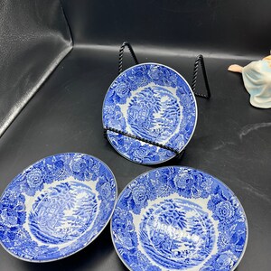 May include: Three blue and white ceramic bowls with a floral pattern and a cottage scene in the center. The bowls are on a black stand.