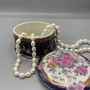 May include: A blue and white porcelain trinket box with a floral design and gold accents. The lid is open and a strand of white pearls is inside.