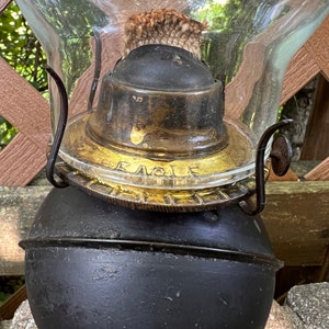 May include: Close-up of an antique oil lamp with a black metal base and a glass chimney. The lamp has a gold-colored metal top with the word "Eagle" inscribed on it.