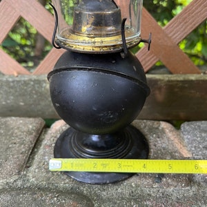 May include: Black oil lamp with a glass chimney and a metal base. The lamp is about 7 inches tall and has a gold-colored trim around the chimney.