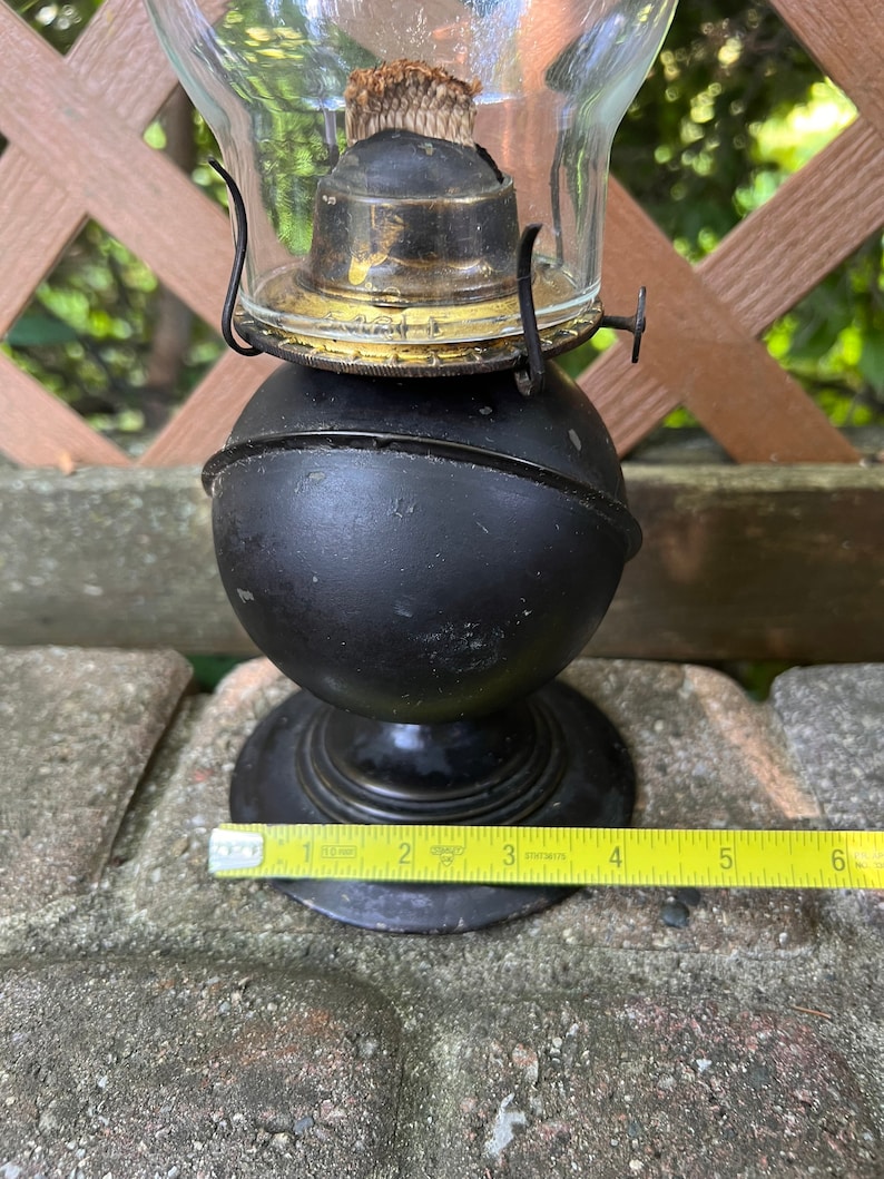 May include: Black oil lamp with a glass chimney and a metal base. The lamp is about 7 inches tall and has a gold-colored trim around the chimney.