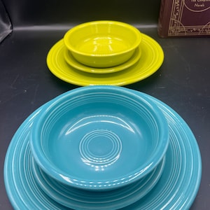 May include: Two sets of Fiestaware dinnerware. One set is turquoise blue with a bowl and two plates. The other set is a bright yellow green with a bowl and a plate.