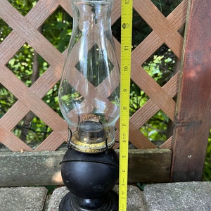 May include: A black oil lamp with a clear glass chimney and a gold-colored metal base. The lamp is about 11 inches tall.
