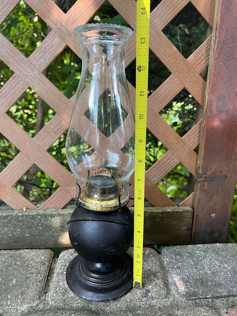 May include: A black oil lamp with a clear glass chimney and a gold-colored metal base. The lamp is about 11 inches tall.
