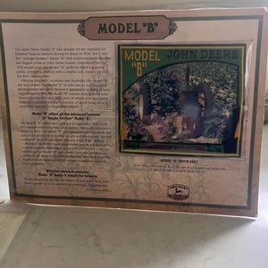 May include: A framed display featuring a John Deere Model "B" tractor patch. The patch is green and yellow with the words "Model John Deere B". The display includes text about the tractor's history and features.