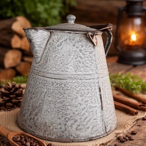 May include: A vintage-style, gray and white speckled enamelware coffee pot with a lid and handle. The pot sits on a burlap cloth with coffee beans, a wooden scoop, and cinnamon sticks. A lit lantern is in the background.
