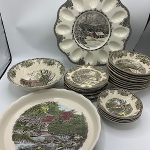 May include: A set of vintage, cream-colored ceramic dishes with a green and brown floral pattern. The set includes a large oval serving dish, a round serving bowl, a smaller round bowl, and a stack of dinner plates.