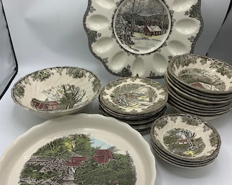 May include: A set of vintage, cream-colored ceramic dishes with a green and brown floral pattern. The set includes a large oval serving dish, a round serving bowl, a smaller round bowl, and a stack of dinner plates.