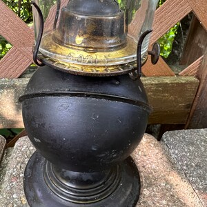 May include: A black and brass oil lamp with a glass chimney. The lamp has a round base and a globe-shaped reservoir. The brass top has the word "Eagle" inscribed on it.