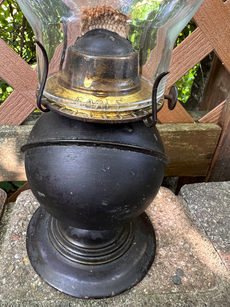 May include: A black and brass oil lamp with a glass chimney. The lamp has a round base and a globe-shaped reservoir. The brass top has the word "Eagle" inscribed on it.