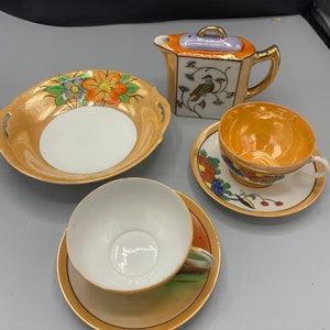 May include: A vintage tea set with a floral design. The set includes a teapot, a sugar bowl, a creamer, and two teacups and saucers. The teacups and saucers are decorated with a bird and floral design. The teapot has a floral design on the side and a bird design on the lid.
