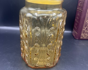 May include: Amber glass jar with a lid and a decorative embossed pattern. The jar is clear and has a textured surface.