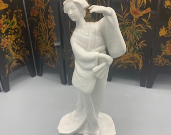 May include: White porcelain figurine of a woman in a traditional Japanese kimono, holding a fan. The figurine is standing on a white base.