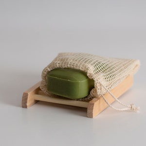May include: A green bar of soap in a white mesh bag, sitting on a wooden soap dish.