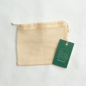 May include: A beige mesh produce bag with a green tag that says "wellbeings" and has a gold line drawing of a plant.
