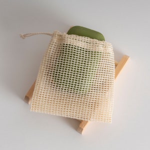 May include: A green bar of soap in a white mesh bag on a wooden stand.