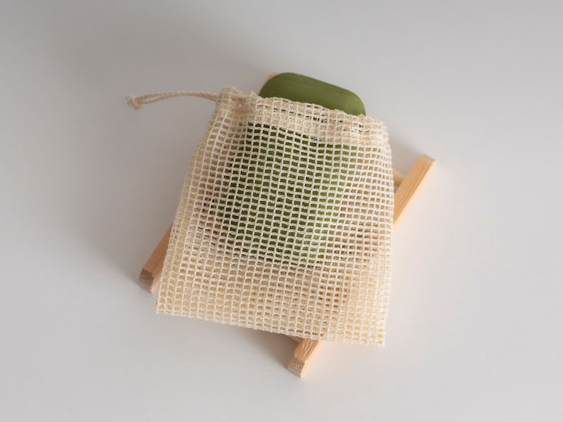 May include: A green bar of soap in a white mesh bag on a wooden stand.