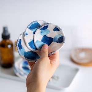 May include: A set of reusable makeup remover pads with a blue and white watercolor pattern. The pads are made of soft, absorbent fabric and are designed to be gentle on the skin.
