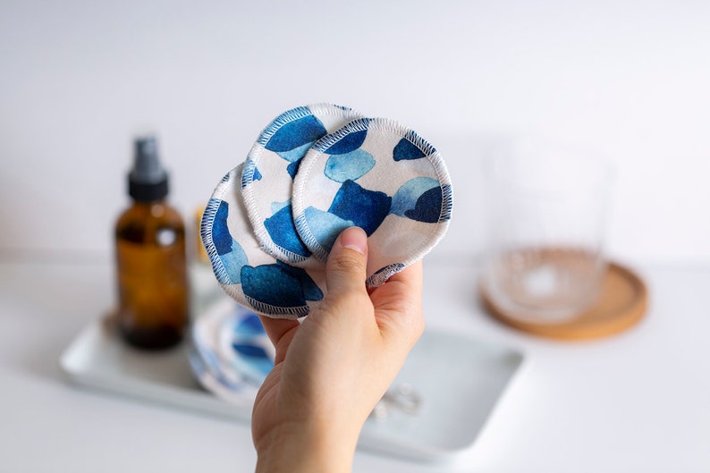 May include: A set of reusable makeup remover pads with a blue and white watercolor pattern. The pads are made of soft, absorbent fabric and are designed to be gentle on the skin.