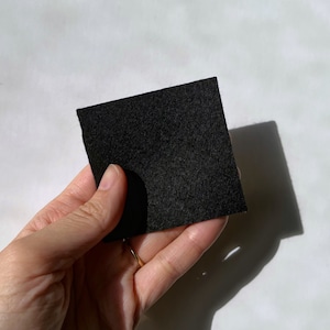 Puede incluir: Un trozo cuadrado de tela de fieltro negro sostenido en una mano.