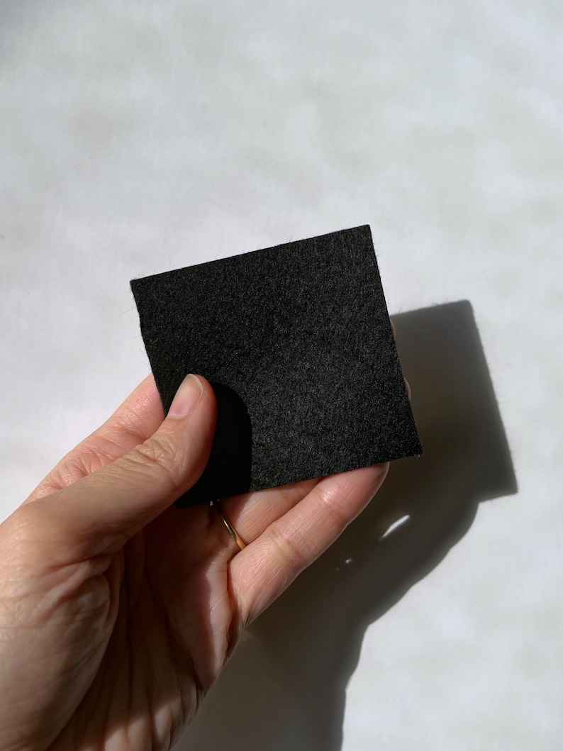 Puede incluir: Un trozo cuadrado de tela de fieltro negro sostenido en una mano.