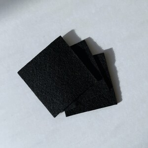 Puede incluir: Tres cuadrados de fieltro negro apilados uno encima del otro.