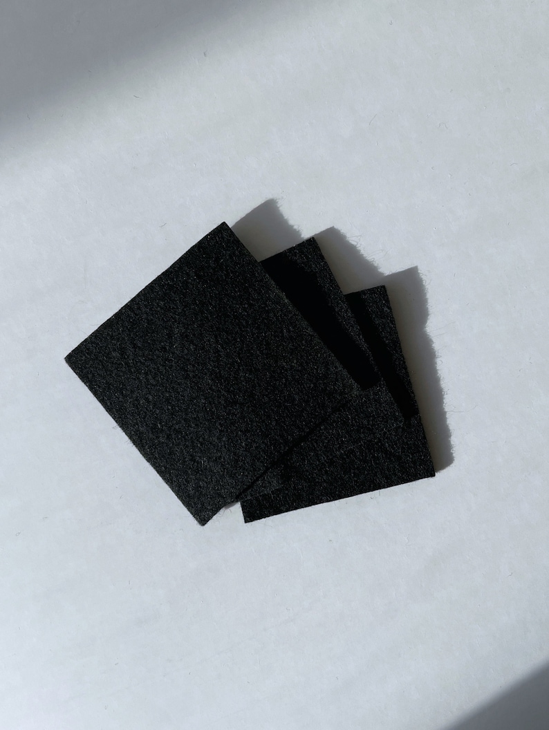 Puede incluir: Tres cuadrados de fieltro negro apilados uno encima del otro.