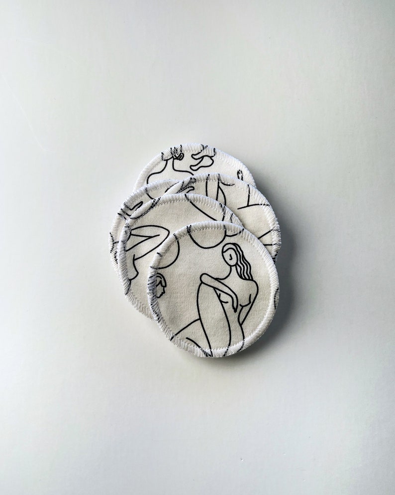 May include: A stack of five white reusable makeup remover pads with a black line drawing of a woman on each pad.