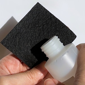 Puede incluir: Una botella de pl&aacute;stico blanca con un cuadrado de fieltro negro colocado sobre la parte superior de la botella.