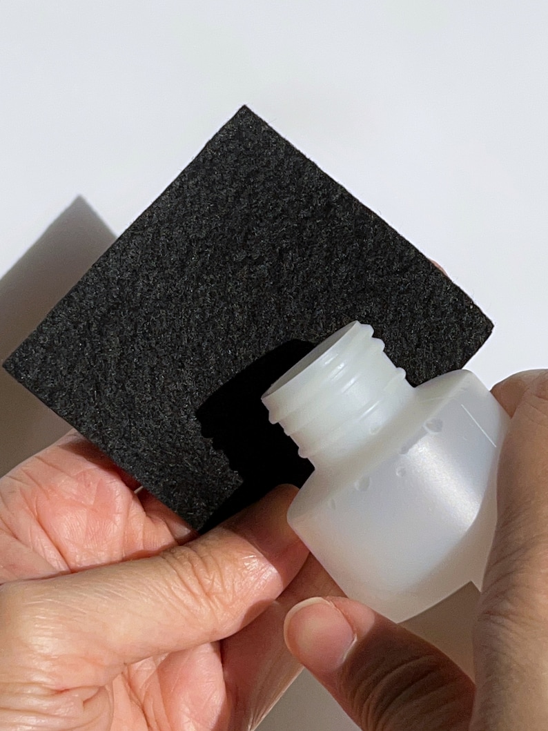 Puede incluir: Una botella de pl&aacute;stico blanca con un cuadrado de fieltro negro colocado sobre la parte superior de la botella.