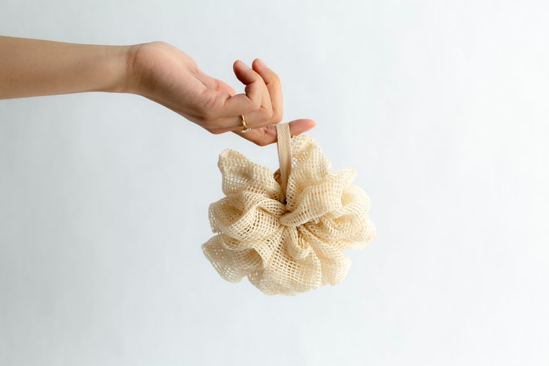 May include: A beige bath pouf with a beige elastic loop. The pouf is made of a soft, mesh material.
